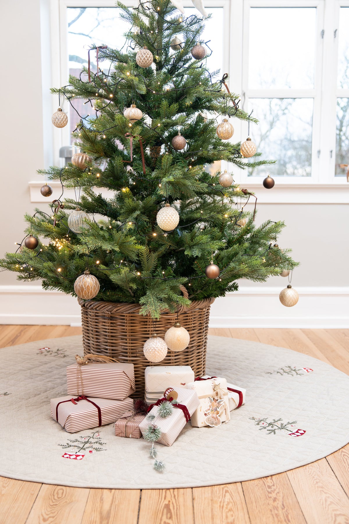 Juletre med pynt i en kurv som står på et quiltet juletreteppe med broderi