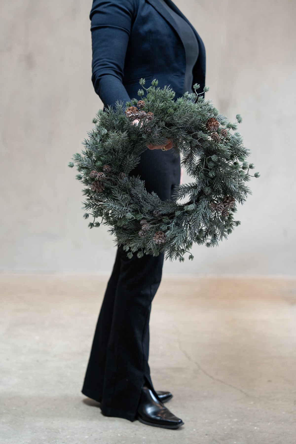 Krans i blandet gran med frost og kongler, 45 cm i diameter, holdt i hånden for å vise målestokk