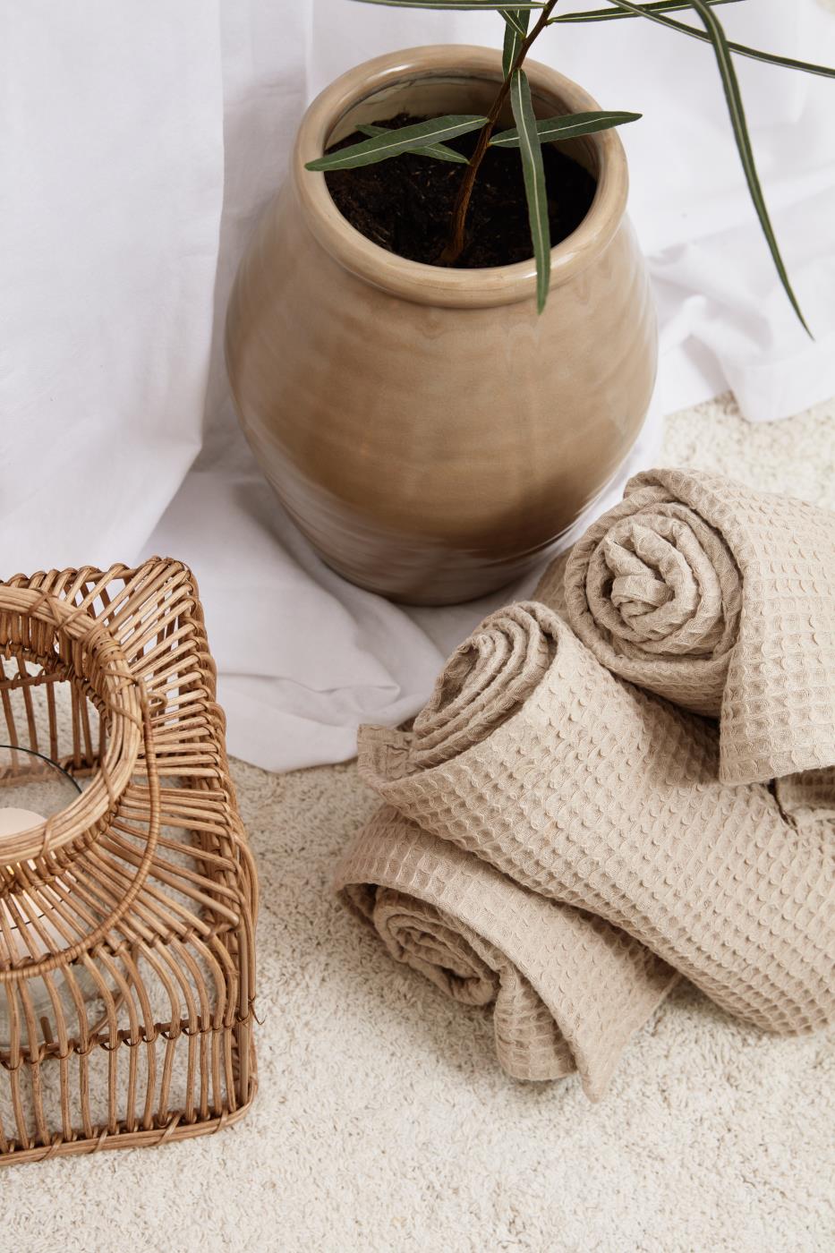 Sammenbrettede beige Liselejehåndklær ved en liten plante og en kurv av naturlige materialer