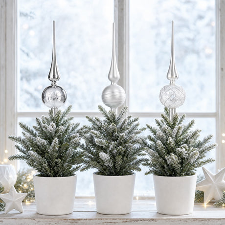 Juletræstop i glas i sølv og hvid pynter på små julegraner i vindueskarm