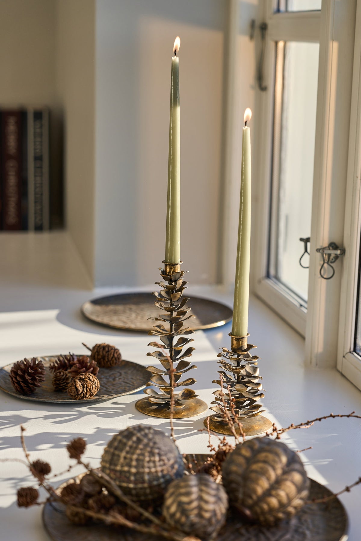 Mønstret dekorasjonsfat i antikk gull med lysestaker, julekuler og naturpynt i en koselig juleoppsetning ved vinduet