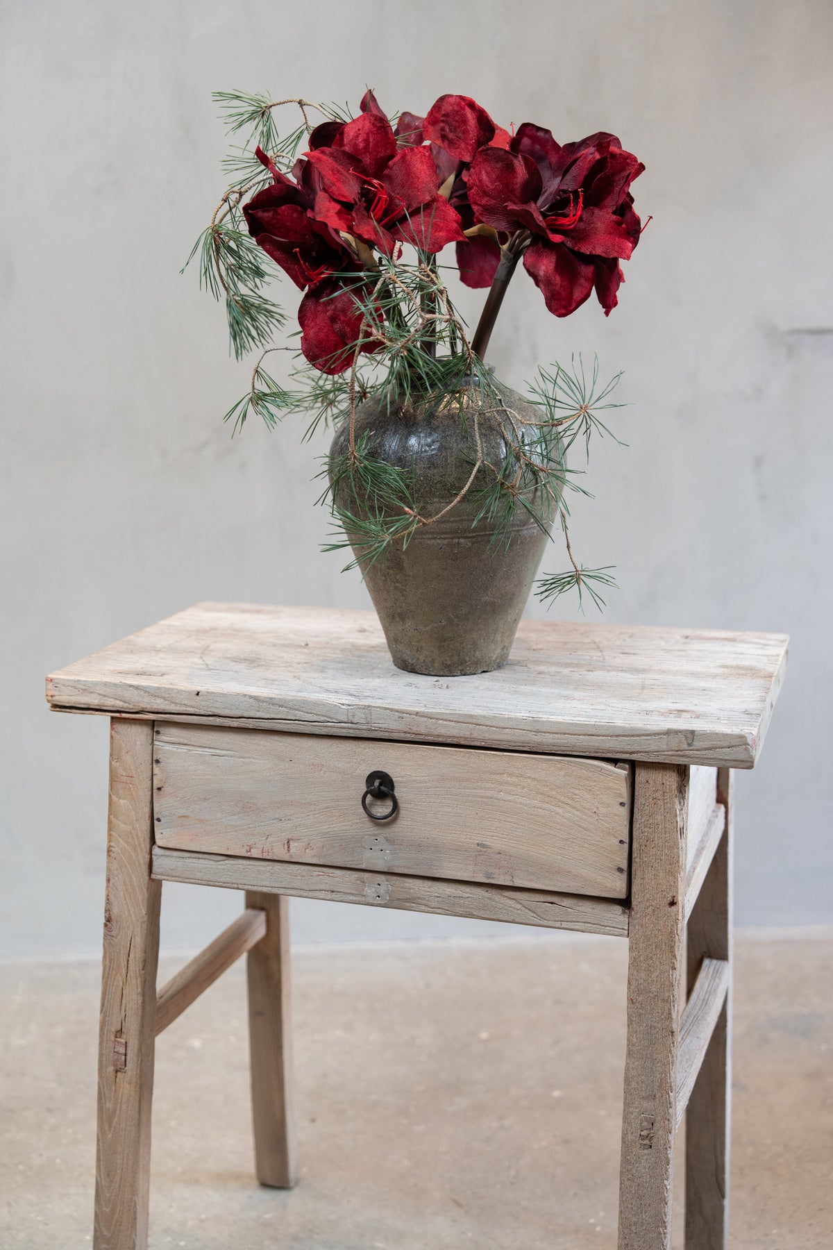 Bukett av kunstige amaryllisstilker med vinrøde blomster og furugreiner i en vase