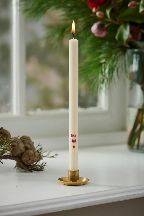 Stearinlys med teksten God jul i gullfarget lysestake på vinduskarmen