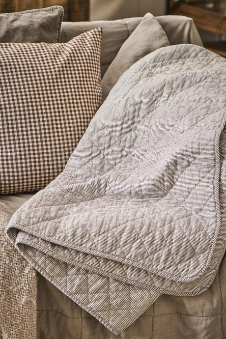 Quilt med hvide og mørkegrå mælkedrengestriber fra Ib Laursen hængende på sofa