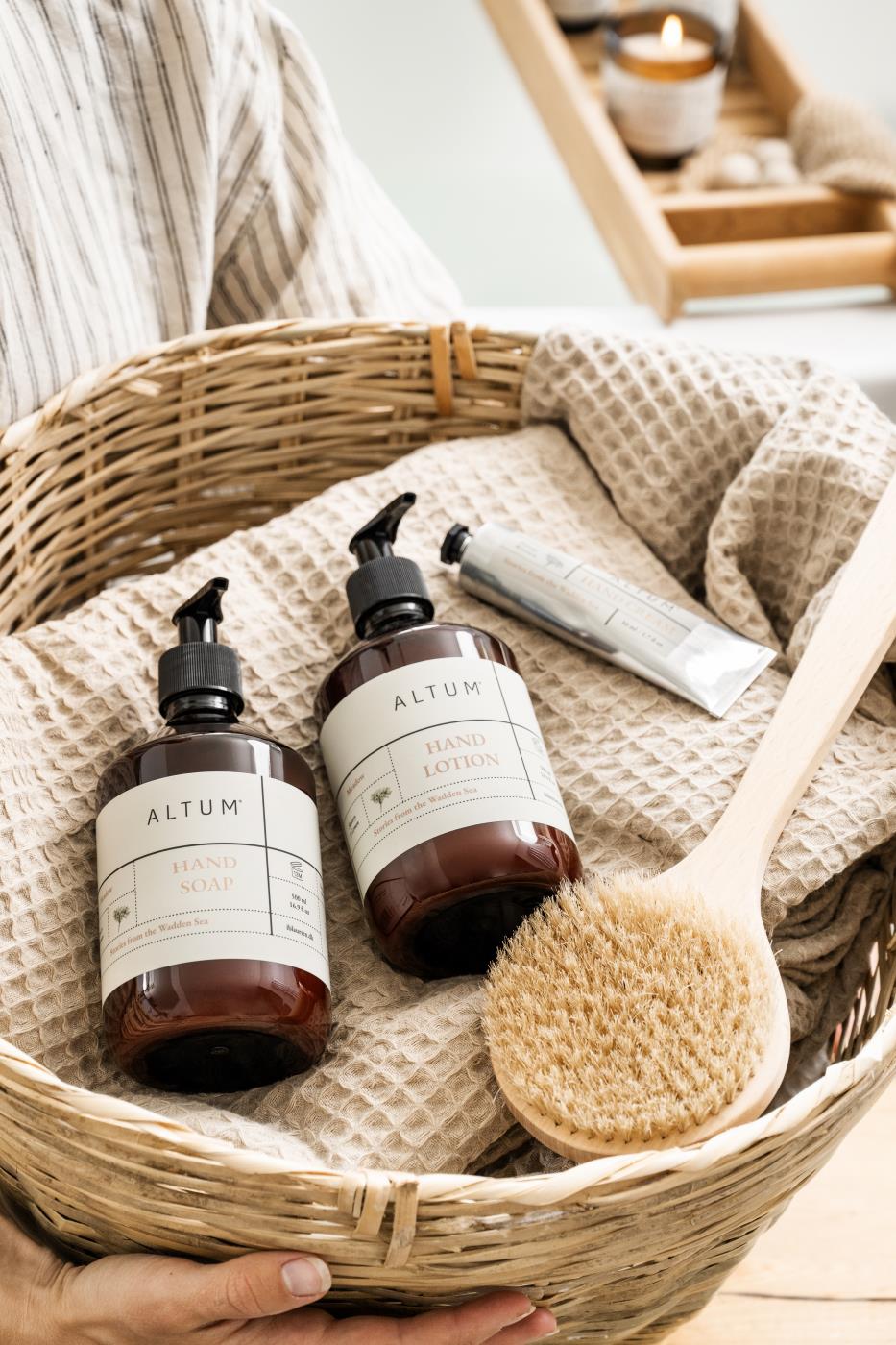 Beige Liseleje håndklær i en flettet kurv sammen med badeprodukter og naturmaterialer